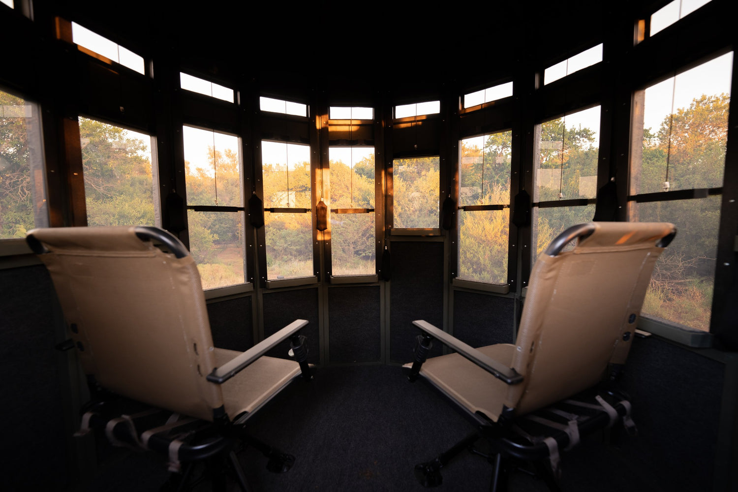 Interior of a 360 Pro XL hunting blind with two chairs and wraparound windows in all directions showing the woods at sunrise