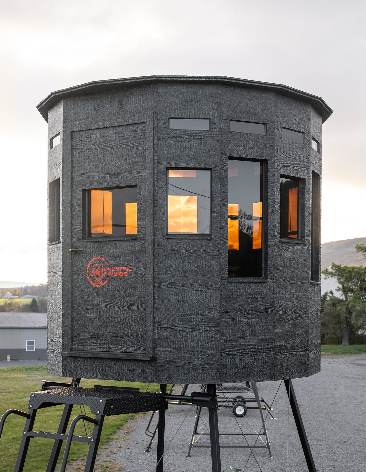 360 Pro XL hunting blind elevated on a tower stand at sunset, windows glowing with the reflected sky