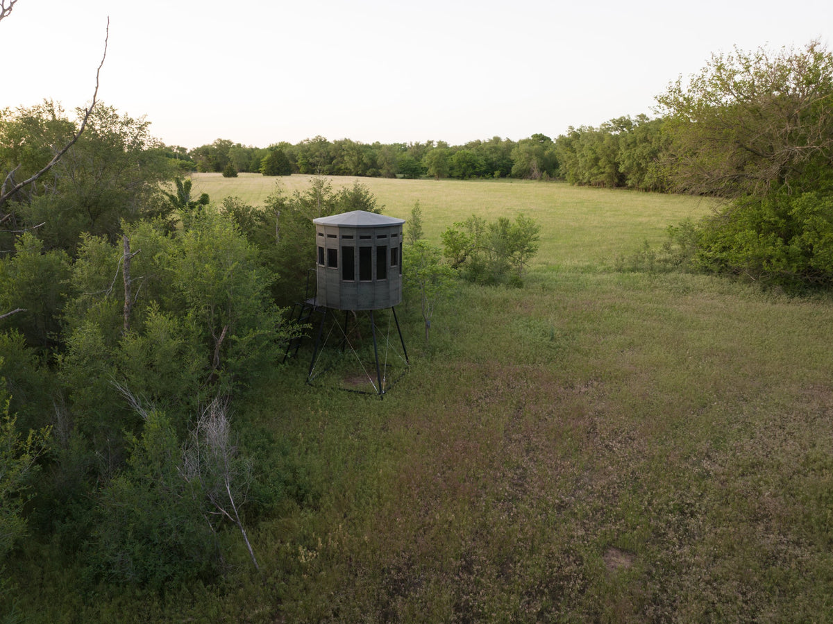 Aerial view of a 360 Pro XL hunting blind on a tower stand set at the edge of a green field and brush