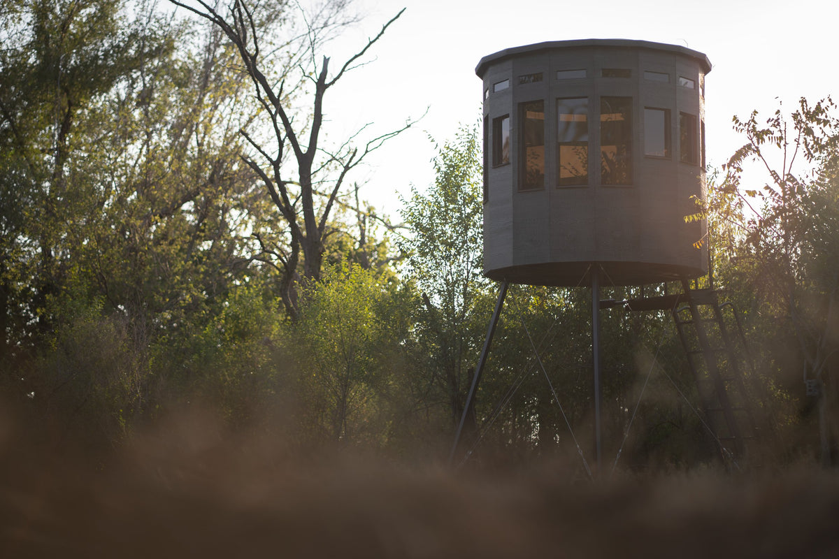 Low-angle view of a 360 Pro XL hunting blind elevated on a tower stand against an evening sky