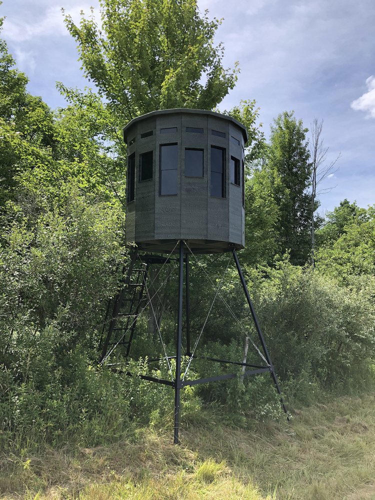 360 Pro hunting blind elevated on a tall tower stand surrounded by green summer foliage