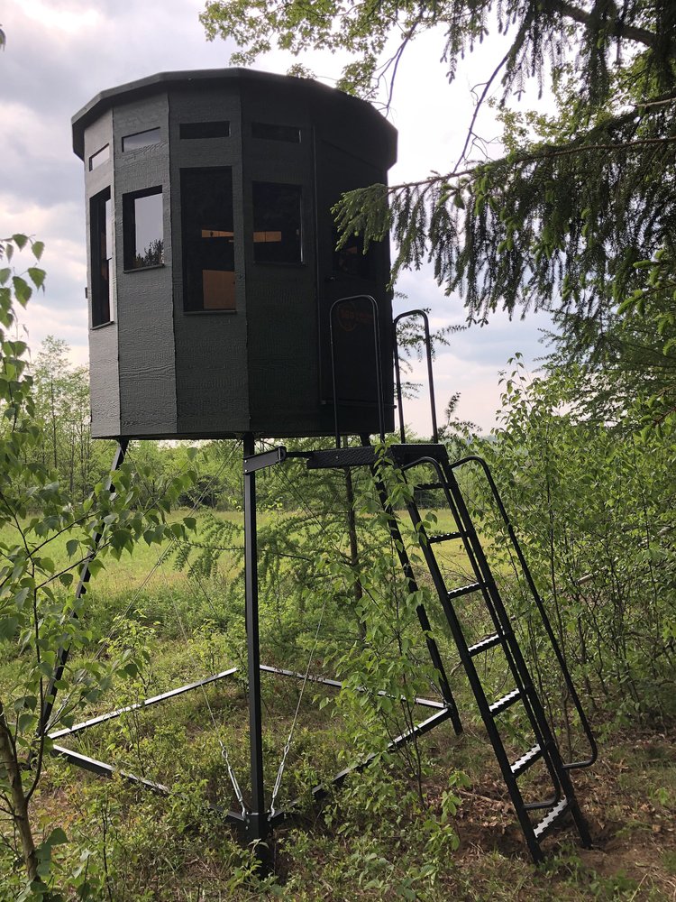 360 Pro hunting blind on a tower stand with a ladder, positioned along a grassy field edge